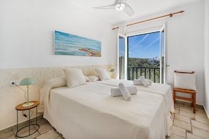 Une chambre avec deux lits, un tableau, un ventilateur de plafond, une fenêtre donnant sur un beau paysage et une chaise.