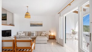 A spacious living room with a sofa, a wooden bench, a TV, and a painting on the wall.