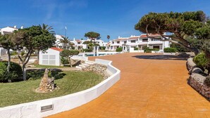 Un resort con un camino pavimentado, edificios blancos y una zona de piscina.