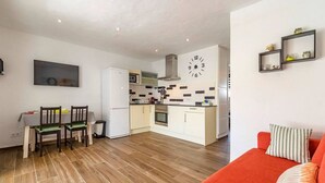 Una cocina moderna con armarios blancos, un microondas y un reloj en la pared. Hay una zona de comedor con una mesa y sillas, y un sofá rojo en la sala de estar.