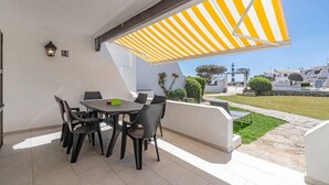 Un patio con una mesa y sillas, un toldo a rayas amarillas y vistas al mar y a edificios.