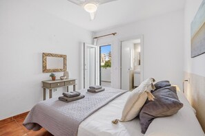 A bedroom with a bed, pillows, a bedside table, a mirror, and a view through an open door. - 3 Bedroom Apartment with great seaviews (Fornells)