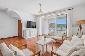 A spacious living room with a TV, sofa, and coffee table, large windows with a view, and a balcony.