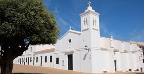 A white building with a bell tower, a large tree in front, and a clear blue sky. - 3 Bedroom Apartment with great seaviews (Fornells)