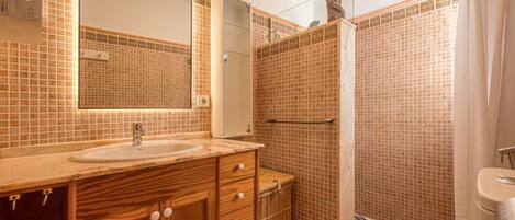 Ein Badezimmer mit einem Holzlagerfläschchen, einem Waschbecken, einem Spiegel, einer Dusche mit gefliesten Wänden und einer Toilette.
