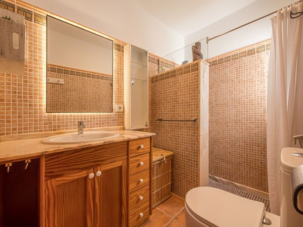A bathroom with a wooden vanity, a sink, a mirror, a shower with tiled walls, and a toilet.