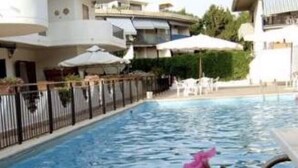 A swimming pool surrounded by a white building with balconies, outdoor umbrellas, and a fence. - Emily Home (Giardini Naxos)