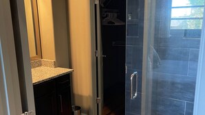 Een moderne badkamer met een douchecabine van glas, donkere betegelde vloer en een granieten aanrechtblad.
