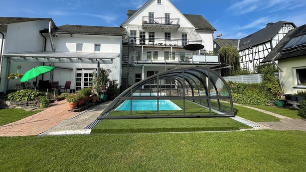 Een woonhuis met een zwembad, een overdekt terras en een groot huis op de achtergrond.