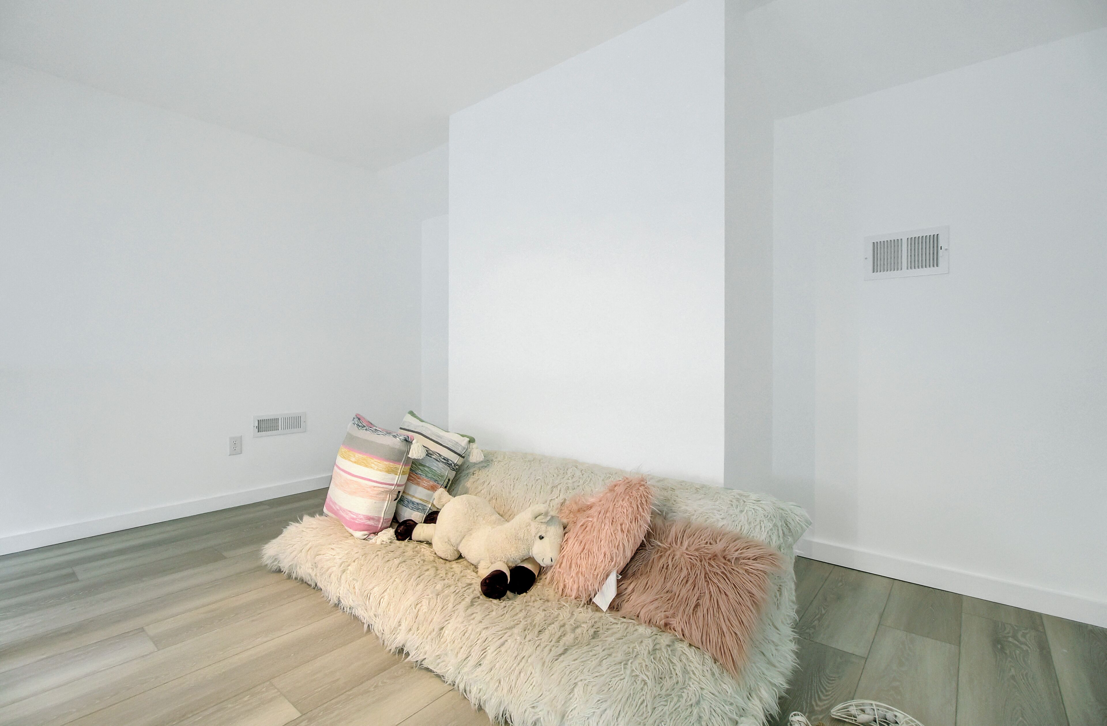 Quarto minimalista com sofá, almofadas fofas e um brinquedo de pelúcia.