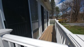 Une terrasse en bois avec des rampes blanches, menant à une porte d’entrée en verre.