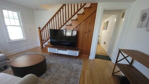 Un salon avec un escalier en bois, un téléviseur à écran plat, une table basse ronde et un tapis à motifs.