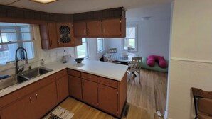 Une cuisine avec des meubles de rangement en bois, un plan de travail blanc et un coin repas comprenant une table et des chaises.
