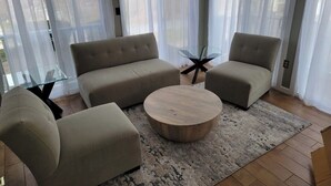 Un salon avec un ensemble de canapés de couleur beige, une table basse en verre et une petite table basse ronde en bois.