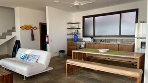 A modern kitchen with a dining area, a white sofa, and a staircase. - Casa Naranja: Ocean View (Puerto Villamil)