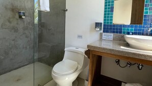 A bathroom with a glass-enclosed shower, a white toilet, and a sink with a wooden countertop. - Casa Naranja: Ocean View (Puerto Villamil)