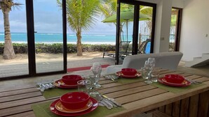 A dining table set with red bowls and wine glasses, overlooking a beach with palm trees and the ocean. - Casa Naranja: Ocean View (Puerto Villamil)