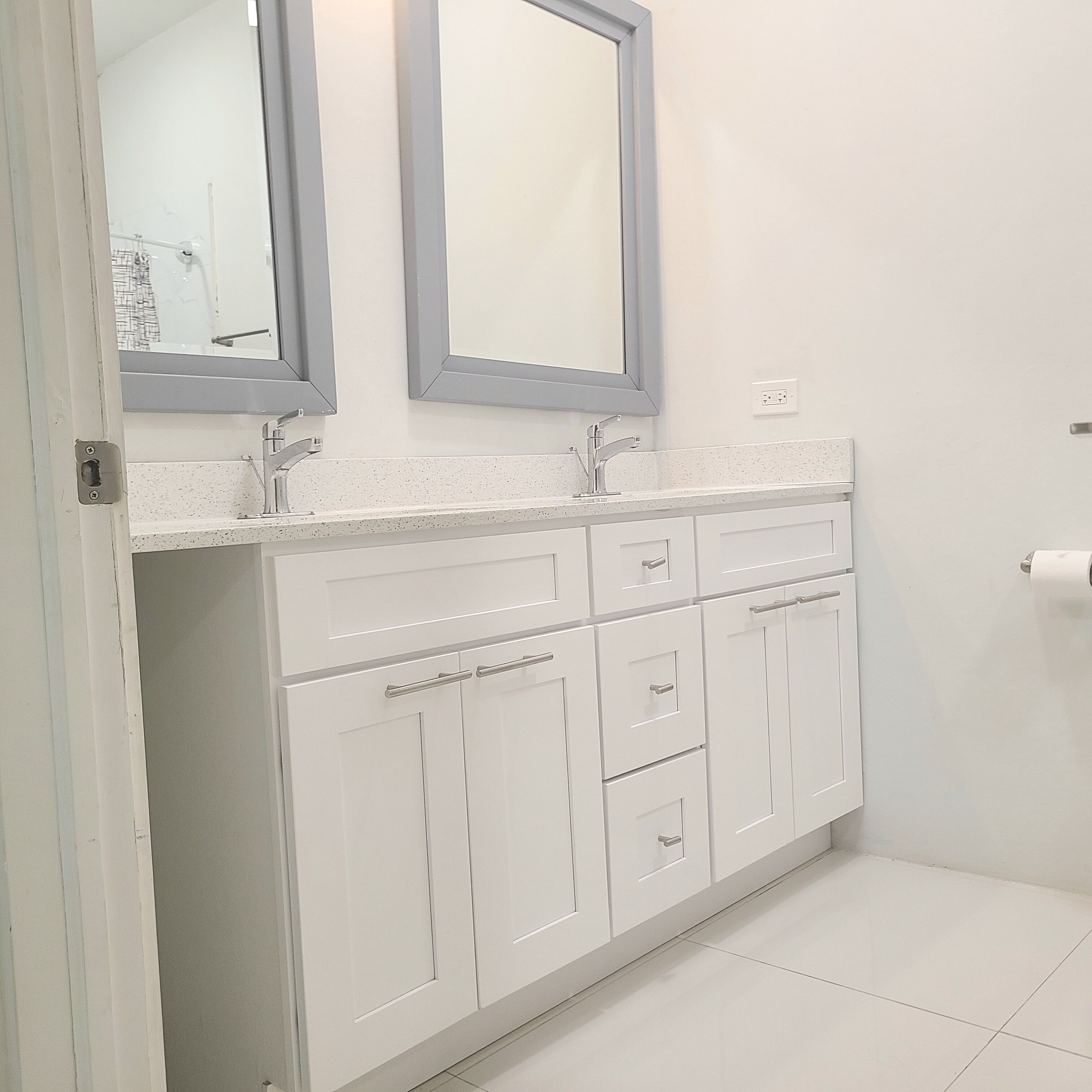Een badkamer met witte kasten, een dubbele wastafel en twee spiegels.