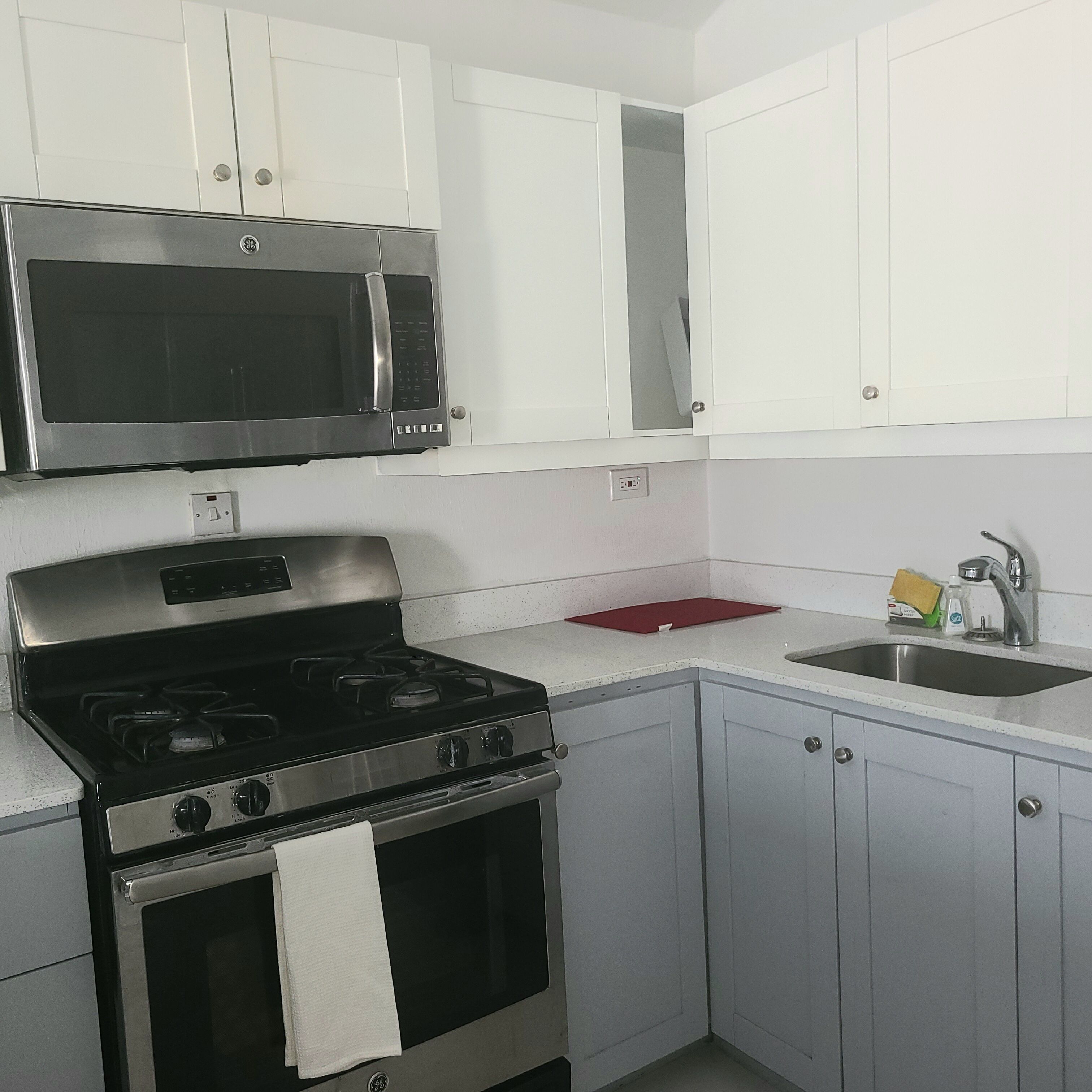 Cocina compacta con armarios blancos, estufa de acero inoxidable, microondas y lavamanos.