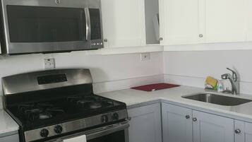 Cocina compacta con armarios blancos, estufa de acero inoxidable, microondas y lavamanos.