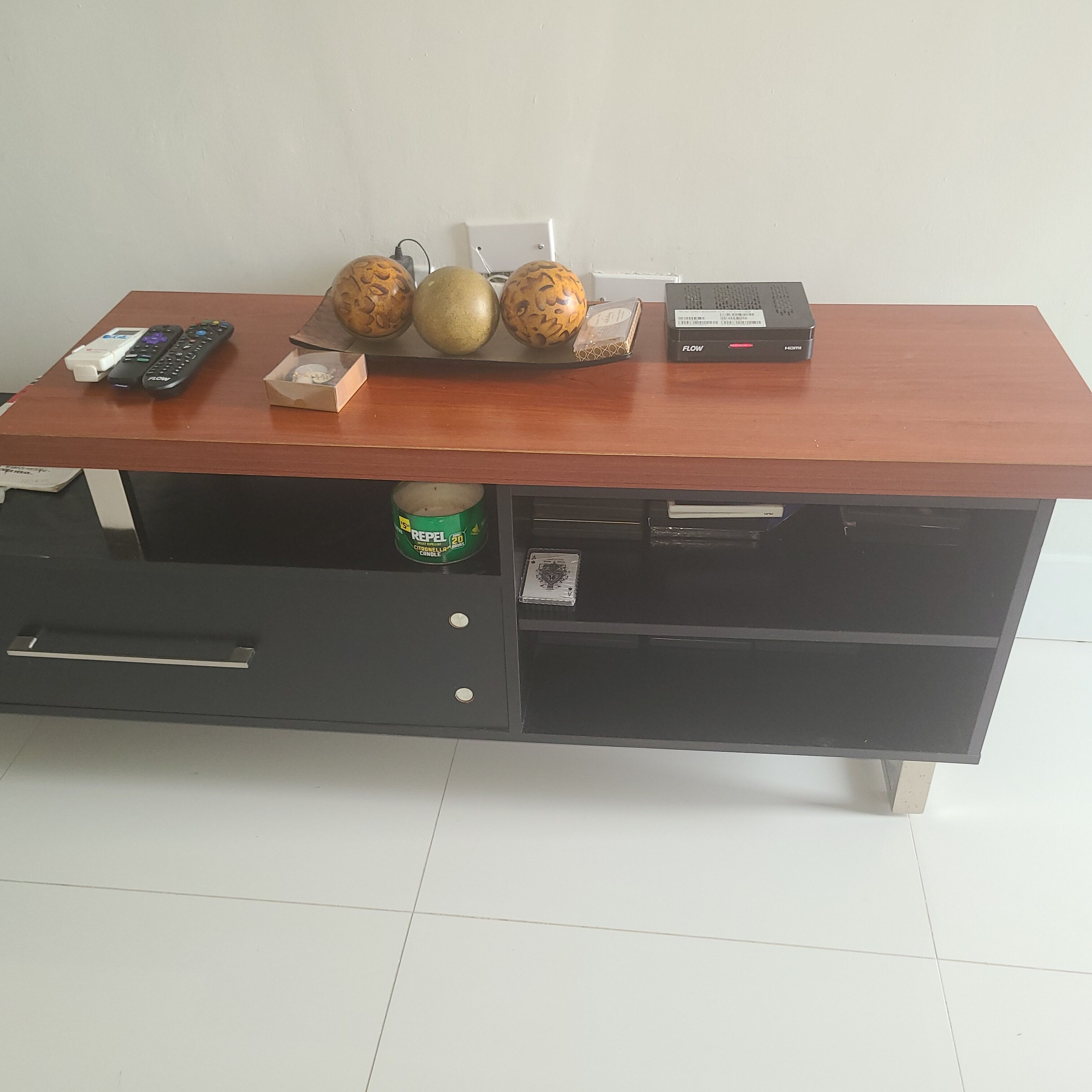 A wooden desk with a remote control, a small box, and a can of Citronella Candle.