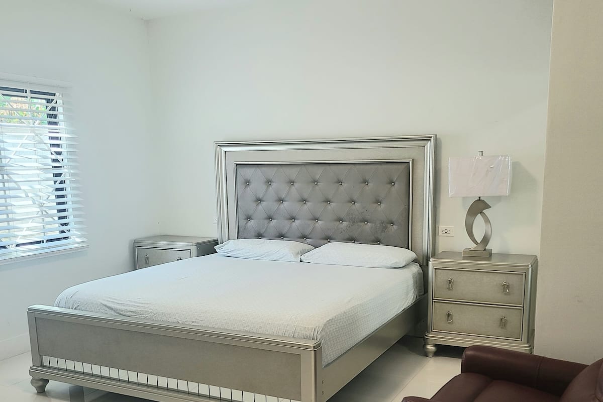 A neatly arranged bedroom with a large bed, a nightstand, a lamp, and a chair.
