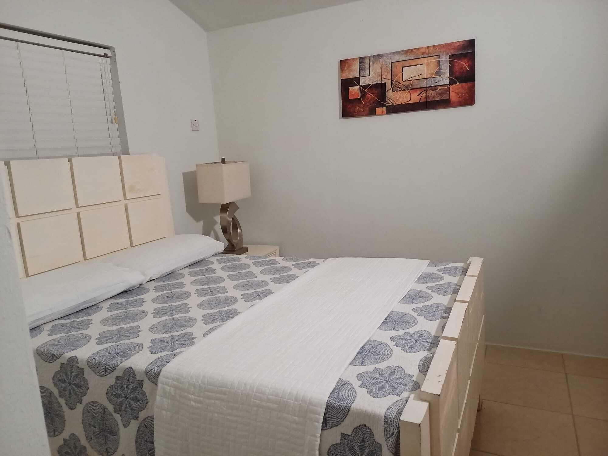 Ein Schlafzimmer mit einem Bett, einem Nachttisch, einer Lampe und einem Wandbild.