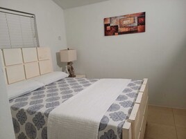 Un dormitorio con cama, mesita de noche, lámpara y una obra de arte en la pared.