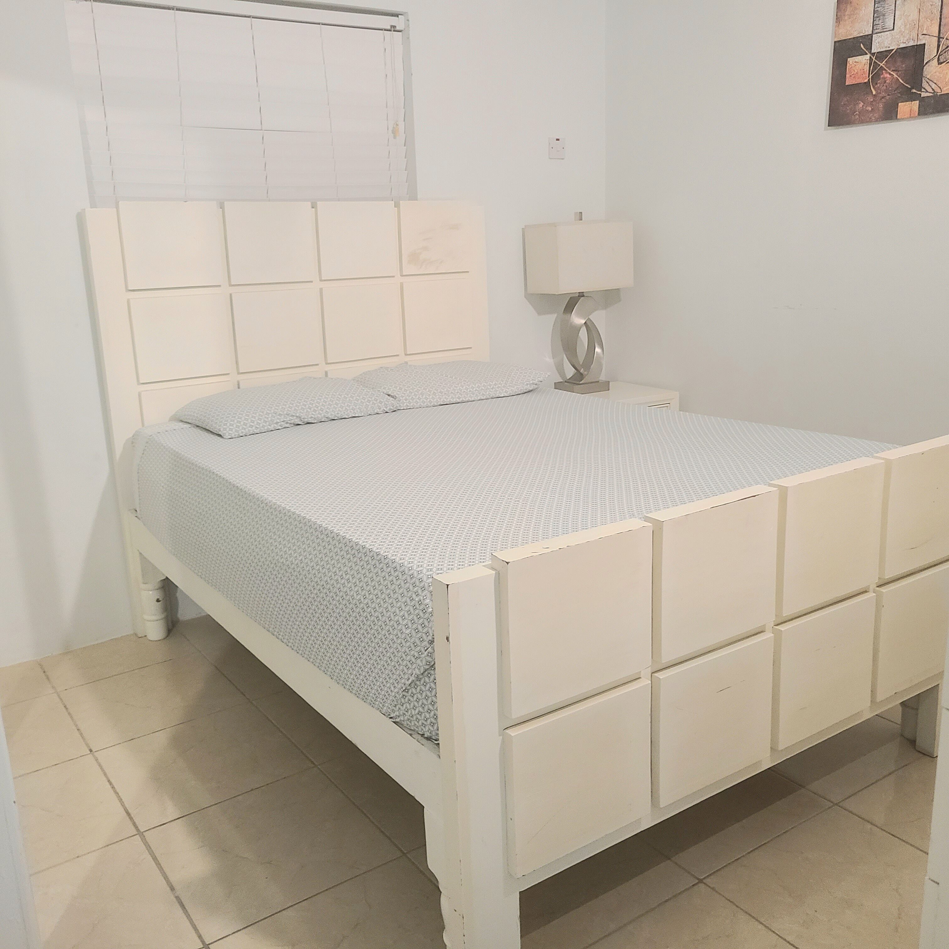 A bed with a headboard, a bedside table with a lamp, and a wall-mounted light switch.
