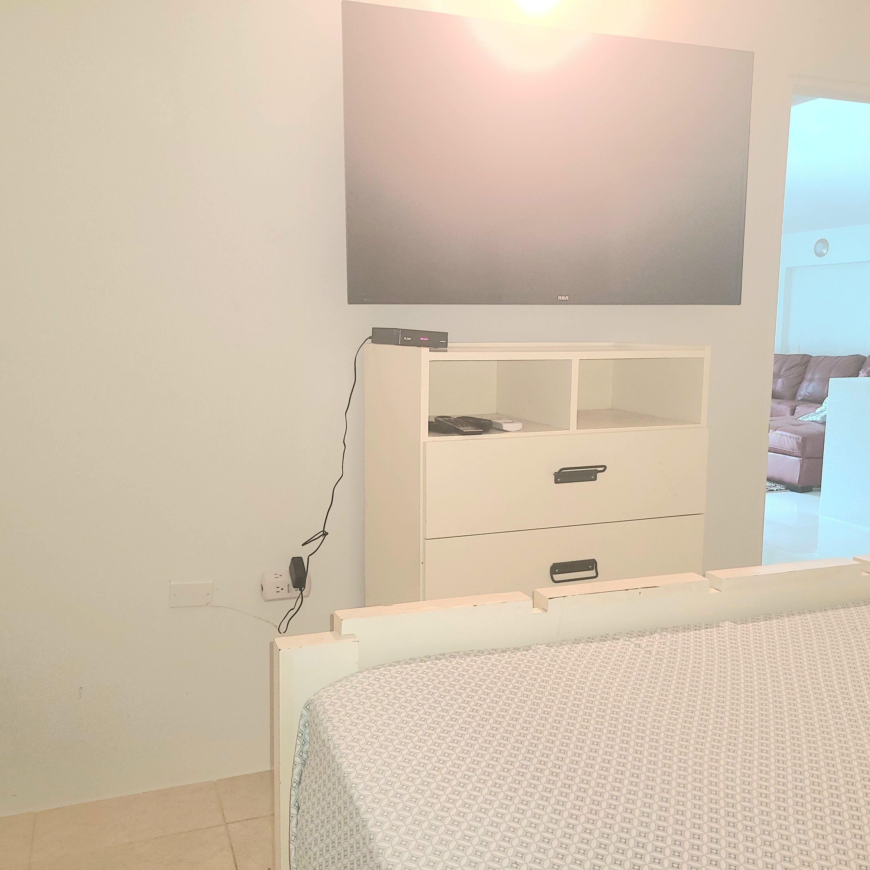 Una camera da letto con un letto, una TV a parete, una cassettiera bianca e una porta che dà su un'altra stanza.