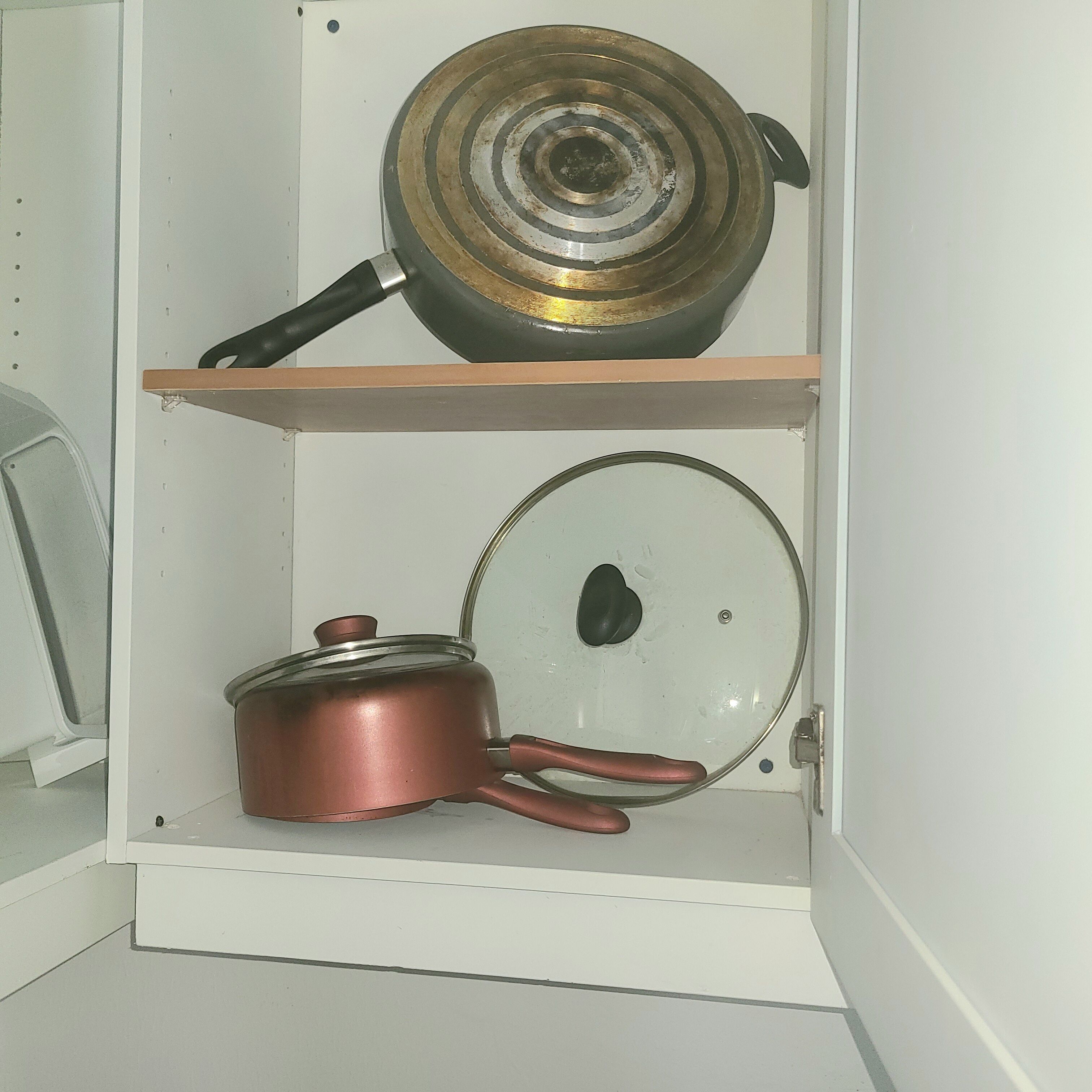 A kitchen cabinet with two shelves, one holding a frying pan and the other a pot.