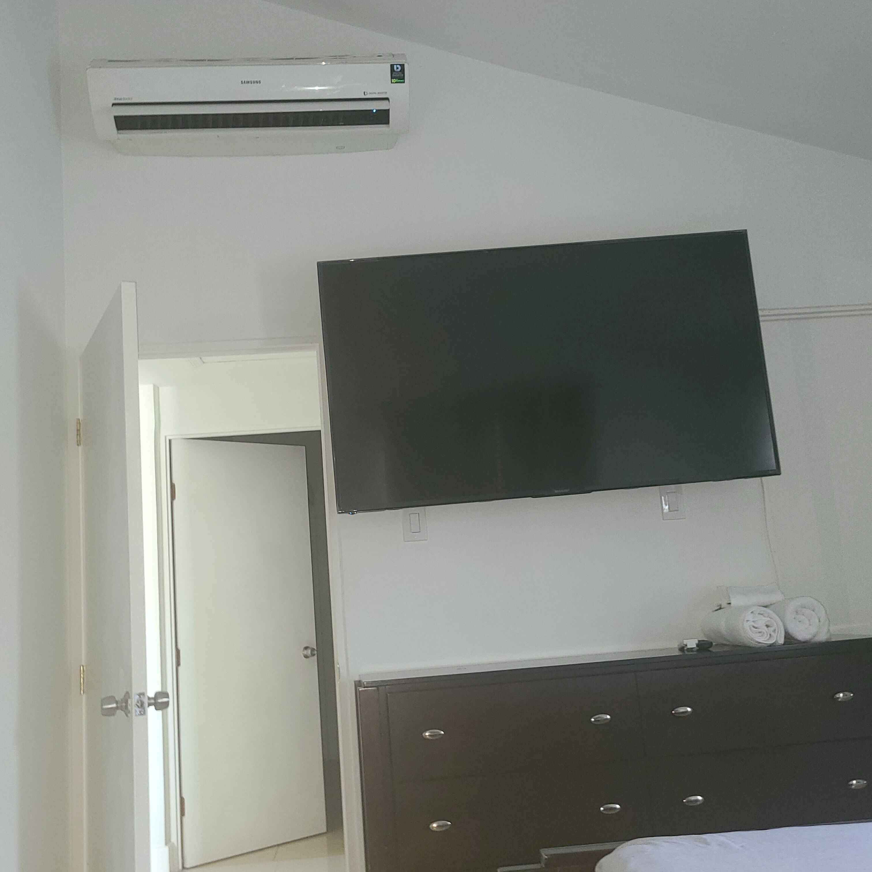 Een slaapkamer met een flatscreen-televisie aan de muur, een donker houten dressoir en een witte deur.