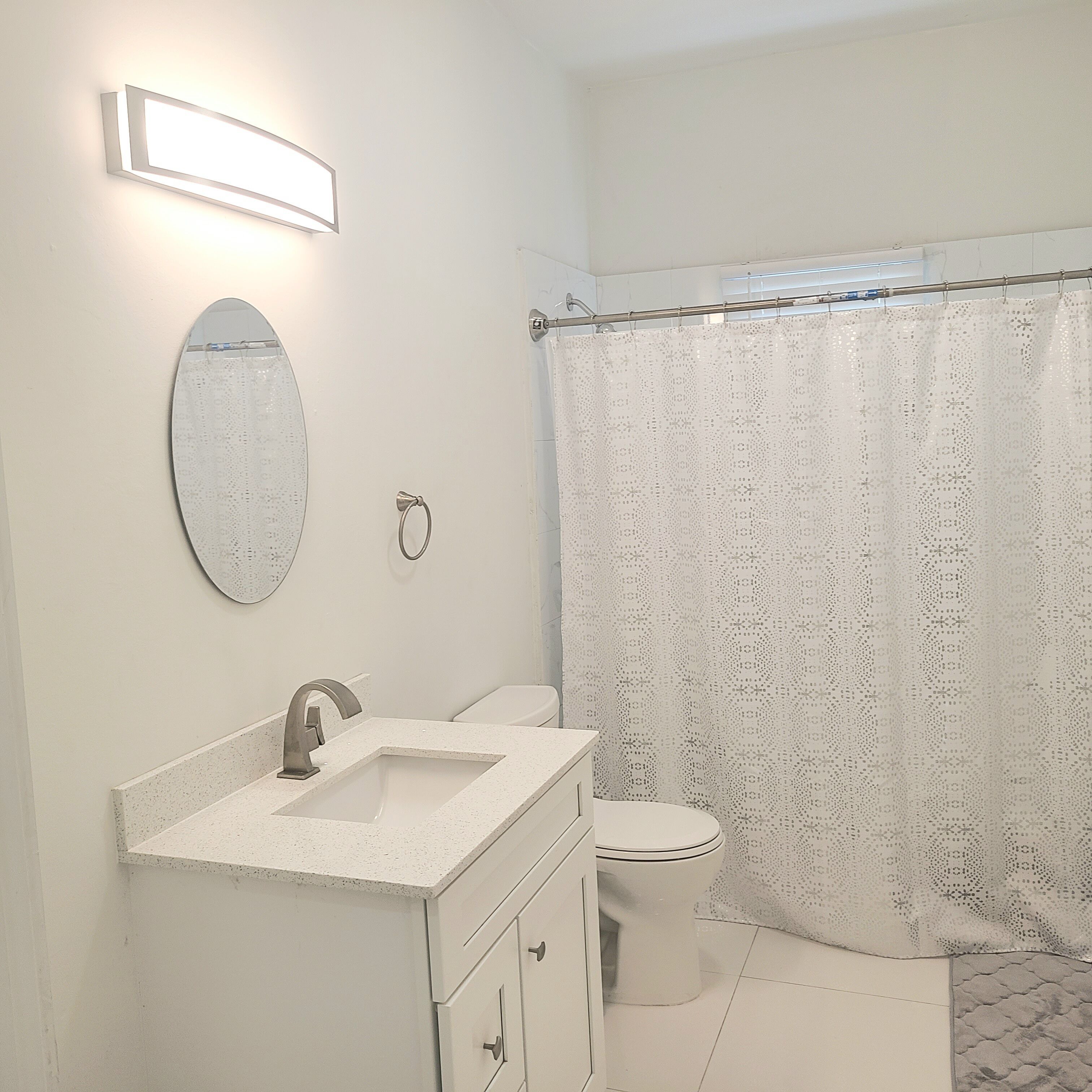 Un baño con lavamanos blanco, espejo, inodoro y cortina de ducha.
