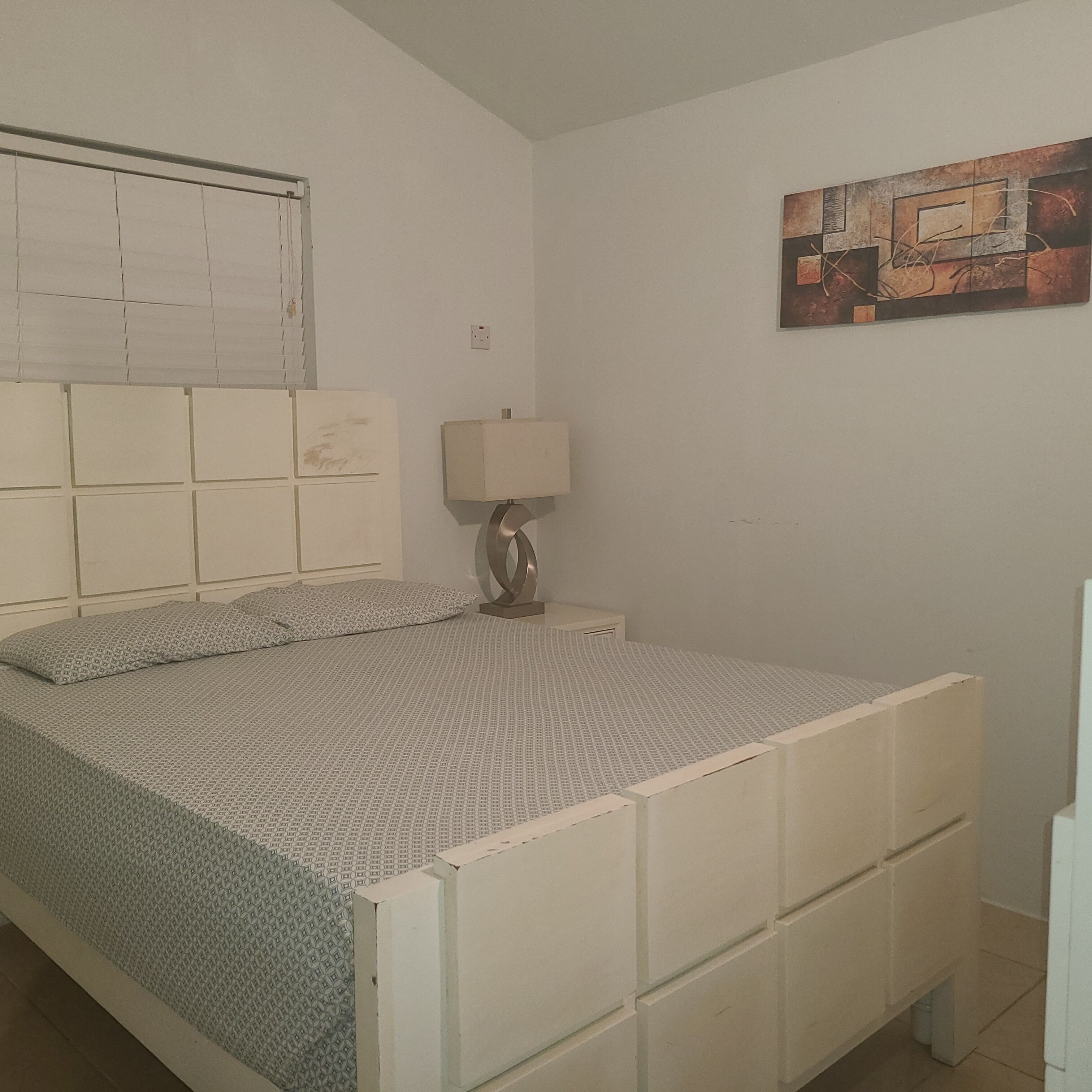 A bedroom with a bed, a nightstand, a lamp, and a painting on the wall.