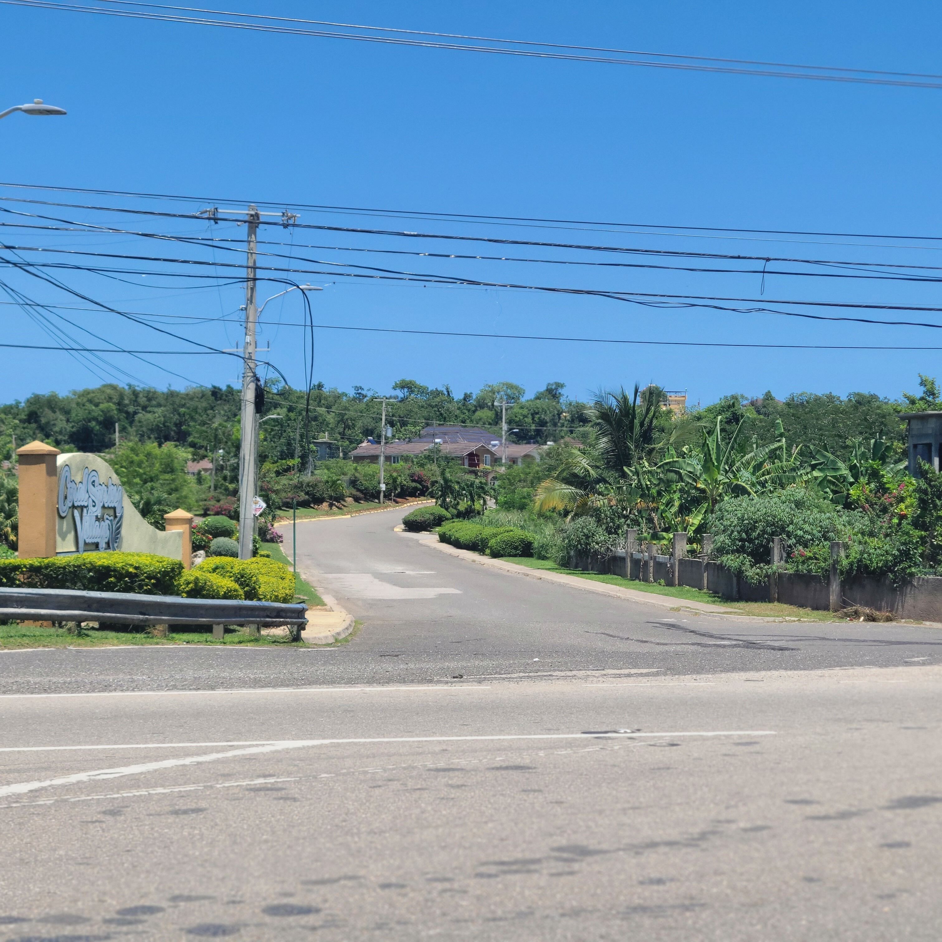 A residential street with a curved road, utility poles, and greenery.