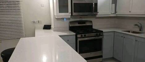 Une cuisine moderne avec des meubles blancs, un four à micro-ondes encastré, une cuisinière et un évier.