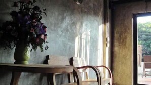 Ein Essbereich mit Holztisch und -stühlen, einer Blumenvase und Blick ins Freie durch ein großes Fenster.