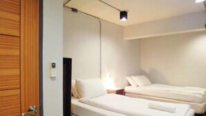 Ein Hotelzimmer mit zwei Einzelbetten, einer Holztür und einem kleinen Nachttisch mit Lampe.