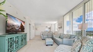 Een ruime woonkamer met een grote flatscreen-tv, een blauwgroene kast en een lichtblauwe zithoek.