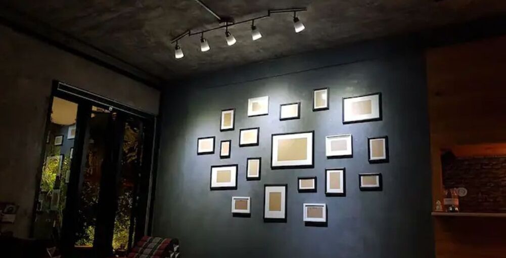 Une pièce dont un mur est peint dans une couleur sombre et orné de tableaux encadrés disposés selon un motif.