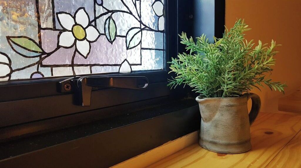 A window with a stained glass design and a potted plant on a wooden surface.