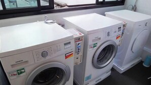 Deux lave-linge à chargement frontal blancs de la marque Siemens se trouvent dans une pièce dotée d’une grande fenêtre.