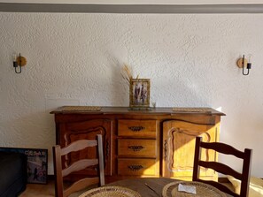 Ein Holztisch mit zwei Stühlen, einer Vase mit Trockenpflanzen und einem gerahmten Bild darauf.