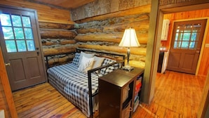 A cozy log cabin room with a bed, a lamp, and a small table.