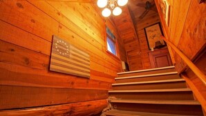 A wooden staircase in a cabin with a flag on the wall and a framed picture above the door.