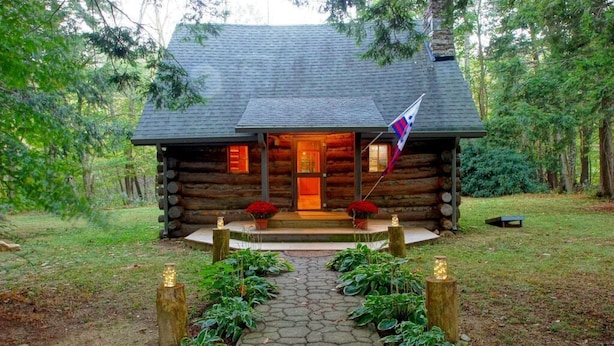 A log cabin with a stone pathway leading to the entrance, surrounded by greenery.