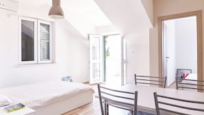 A bright, modern bedroom with a bed, bedside table, and a dining area with chairs.