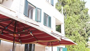 A two-story building with a patio area featuring a wooden table and chairs under a red umbrella.