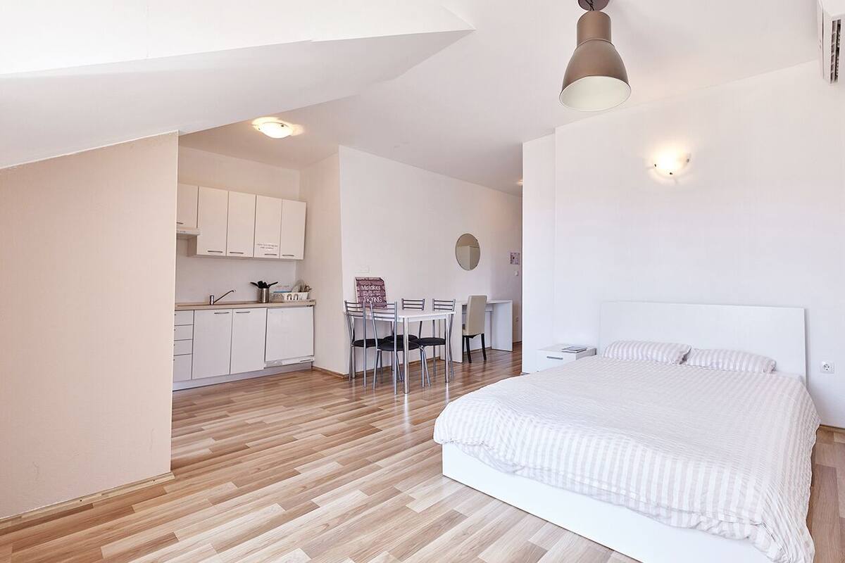 Camera moderna con un letto grande, un'area pranzo con tavolo e sedie e una cucina sullo sfondo.
