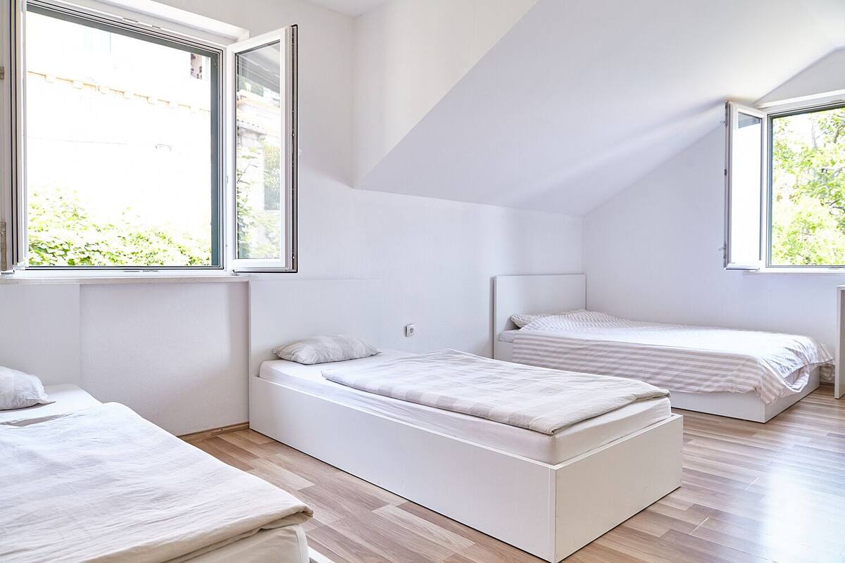 Una camera da letto moderna e minimalista con due letti, ampie finestre e un soffitto spiovente.
